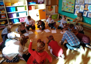 Dzieci z grupy Wiewiórek siedzą w kole na podłodze. Przed nimi leżą kartony. Przedszkolaki kolorowymi mazakami rysują śmieszne misie.